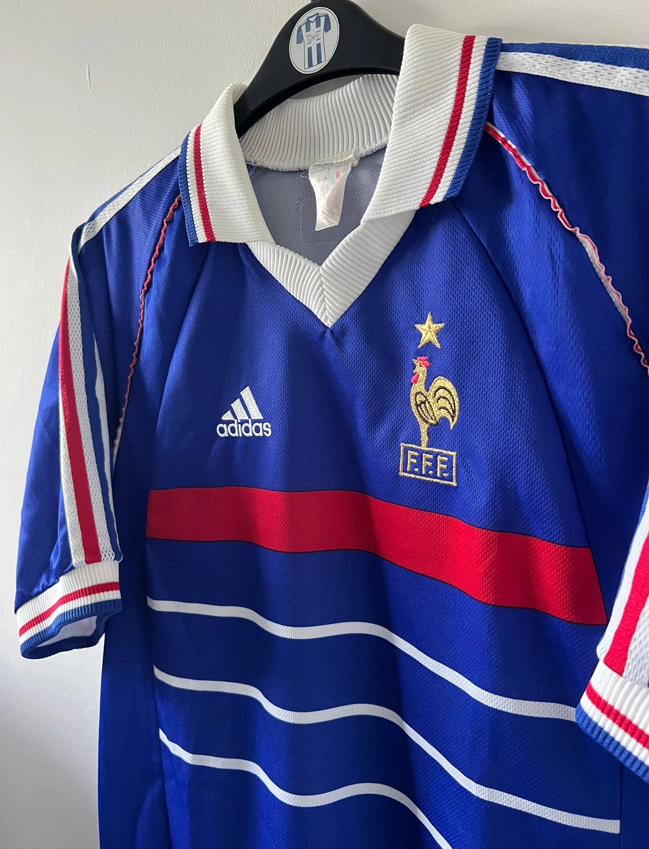 Maillot de foot vintage domicile bleu blanc et rouge de l'équipe de france 1998. On peut retrouver l'équipementier Adidas. Le maillot est floqué du numéro 10 Zinedine Zidane. Il s'agit d'un maillot authentique d'époque.