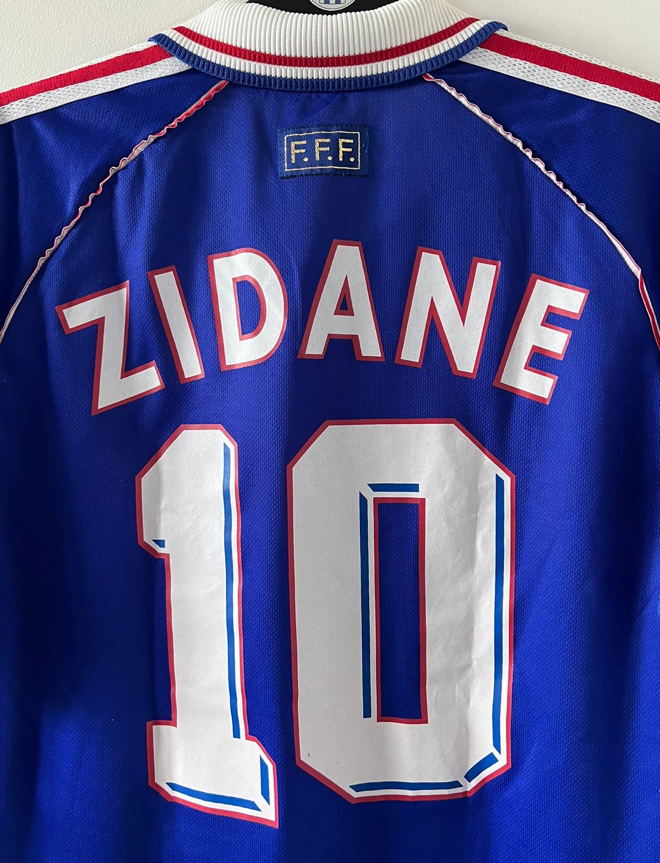 Maillot de foot vintage domicile bleu blanc et rouge de l'équipe de france 1998. On peut retrouver l'équipementier Adidas. Le maillot est floqué du numéro 10 Zinedine Zidane. Il s'agit d'un maillot authentique d'époque.