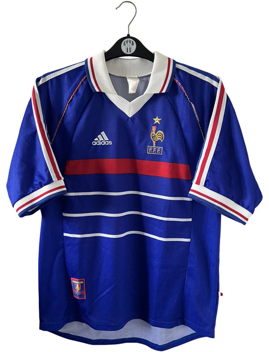 Maillot de foot vintage domicile bleu blanc et rouge de l'équipe de france 1998. On peut retrouver l'équipementier Adidas. Le maillot est floqué du numéro 10 Zinedine Zidane. Il s'agit d'un maillot authentique d'époque.