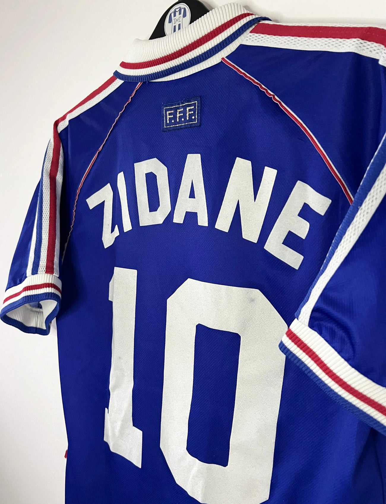 Maillot de foot vintage domicile bleu de l'Equipe de France 1998. On peut retrouver l'équipementier Adidas. Le maillot est floqué Zinedine Zidane. Il s'agit d'un maillot authentique d'époque.