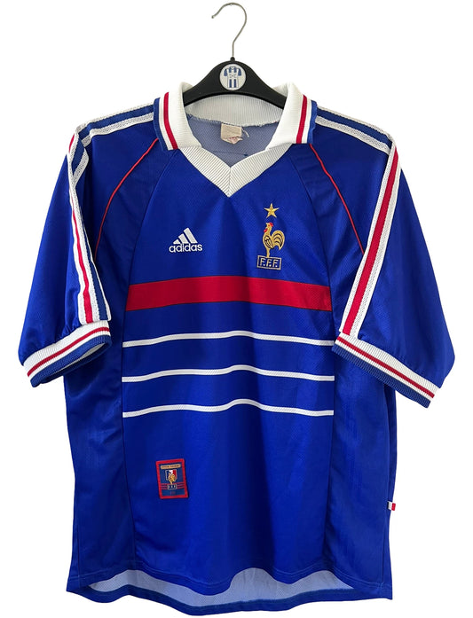Maillot de foot vintage domicile bleu de l'équipe de france 1998. On peut retrouver l'équipementier Adidas. Le maillot est floqué du numéro 10 Zinedine Zidane. Il s'agit d'un maillot authentique d'époque.