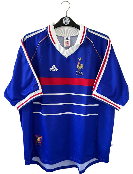 Maillot de foot vintage domicile bleu de l'équipe de france 1998. On peut retrouver l'équipementier Adidas. Le maillot est floqué du numéro 10 Zinedine Zidane. Il s'agit d'un maillot authentique d'époque.