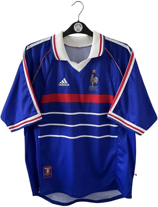 Maillot de foot vintage domicile bleu de l'équipe de france 1998. On peut retrouver l'équipementier Adidas. Le maillot est floqué du numéro 10 Zinedine Zidane. Il s'agit d'un maillot authentique d'époque.