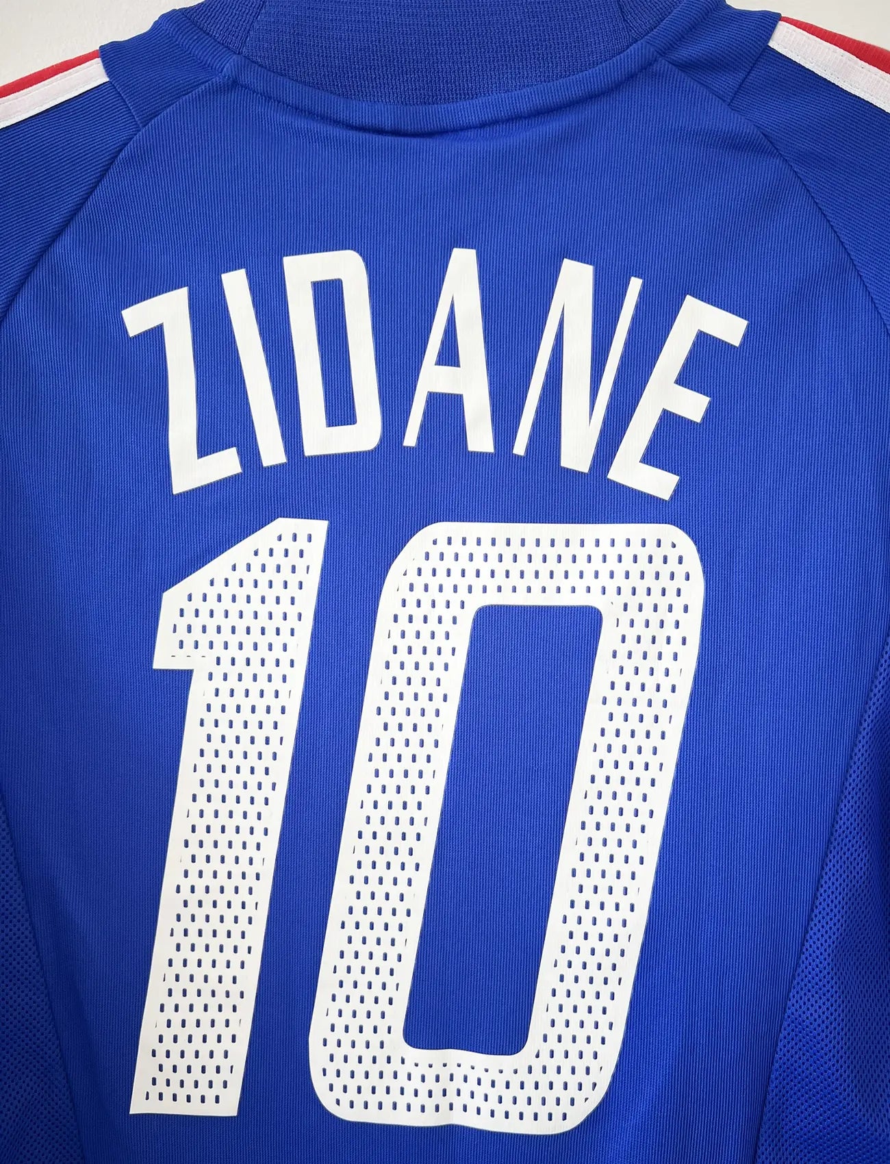 Maillot de foot vintage domicile de l'équipe de france 2002. Le maillot est de couleur bleu blanc et rouge. On peut retrouver l'équipementier adidas. Le maillot est floqué du numéro 10 Zinedine Zidane. Il s'agit d'un maillot authentique d'époque comportant les numéros 139531.