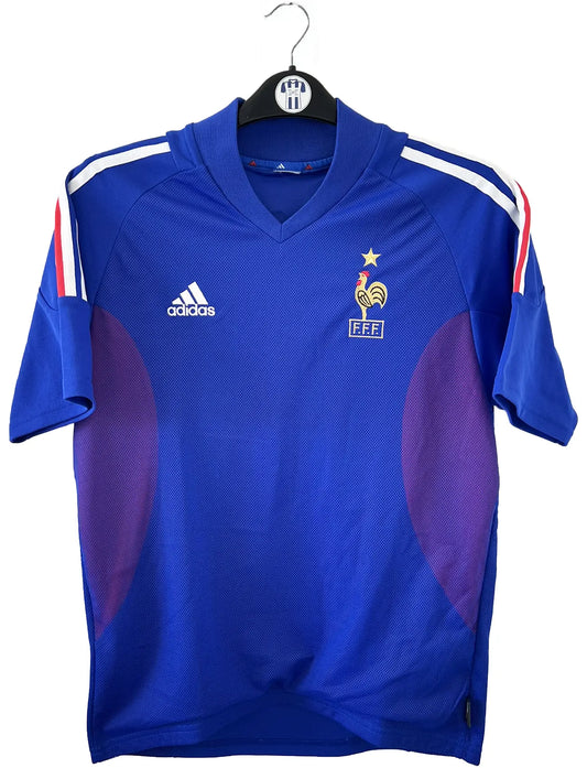 Maillot de foot vintage domicile de l'équipe de france 2002. Le maillot est de couleur bleu blanc et rouge. On peut retrouver l'équipementier adidas. Le maillot est floqué du numéro 10 Zinedine Zidane. Il s'agit d'un maillot authentique d'époque comportant les numéros 139531.