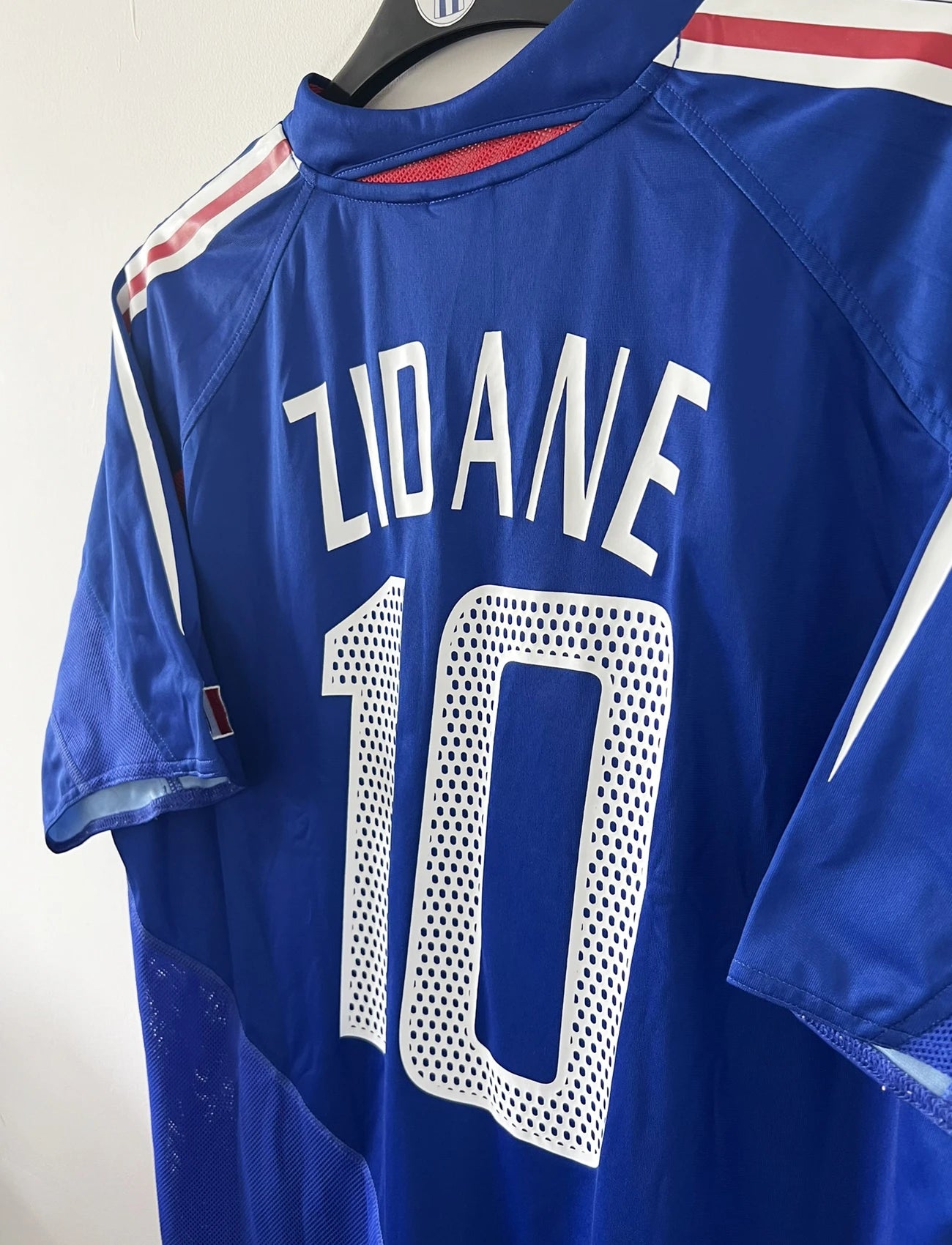 Maillot de foot vintage domicile de l'équipe de france 2004/2006. On peut retrouver l'équipementier adidas. Le maillot est floqué du numéro 10 Zinedine Zidane. Il s'agit d'un maillot authentique d'époque comportant l'étiquette 600222.