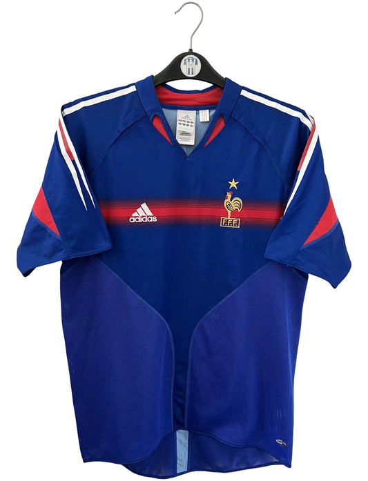 Maillot de foot vintage domicile bleu de l'équipe de france 2004. On peut retrouver l'équipementier Adidas. Le maillot est floqué du numéro 10 Zinedine Zidane. Il s'agit d'un maillot authentique d'époque.