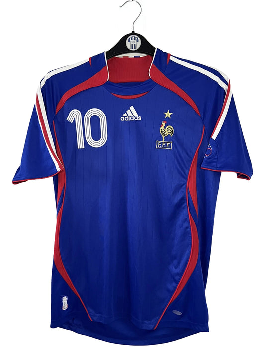 Maillot de foot vintage domicile bleu de l'équipe de france 2006. On peut retrouver l'équipementier Adidas. Le maillot est floqué du numéro 10 Zinedine Zidane. Il s'agit d'un maillot authentique d'époque comportant l'étiquette 740126.