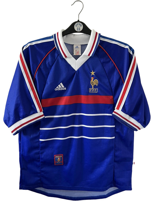 Maillot de foot vintage domicile bleu de l'équipe de france 1998. On peut retrouver l'équipementier Adidas. Le maillot est floqué du numéro 10 Zinedine Zidane. Il s'agit d'un maillot authentique d'époque.