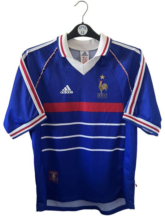 Maillot de foot vintage domicile bleu de l'équipe de france 1998. On peut retrouver l'équipementier Adidas. Le maillot est floqué du numéro 10 Zinedine Zidane. Il s'agit d'un maillot authentique d'époque.