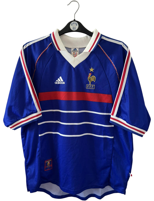 Maillot de foot vintage domicile bleu de l'équipe de France 1998. On peut retrouver l'équipementier Adidas. Le maillot est floqué du numéro 10 Zinedine Zidane. Il s'agit d'un maillot authentique d'époque.