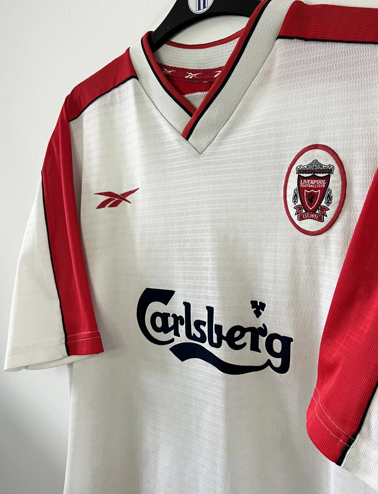 Maillot foot vintage extérieur liverpool blanc et rouge de la saison 1999/2000. On peut retrourver l'équipementier reebok et le sponsor carlsberg. Le maillot est floqué du numéro 10 Michael Owen. Il s'agit d'un maillot authentique d'époque.