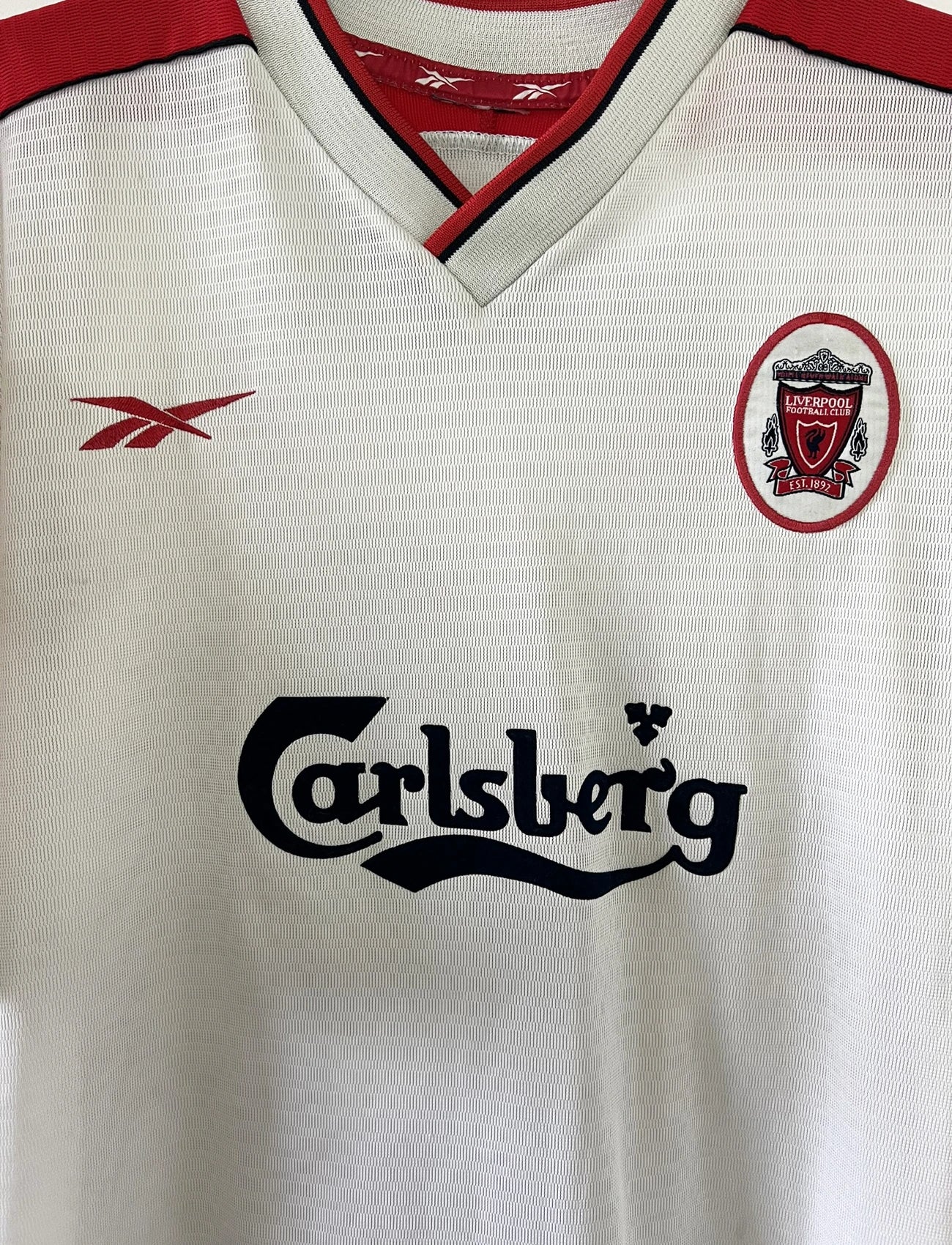 Maillot foot vintage extérieur liverpool blanc et rouge de la saison 1999/2000. On peut retrourver l'équipementier reebok et le sponsor carlsberg. Le maillot est floqué du numéro 10 Michael Owen. Il s'agit d'un maillot authentique d'époque.