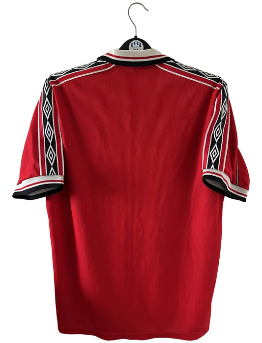 Maillot de foot vintage domicile rouge de Manchester United saison 1998/2000. On peut retrouver l'équipementier Umbro et le sponsor Sharp. Il s'agit d'un maillot authentique d'époque.