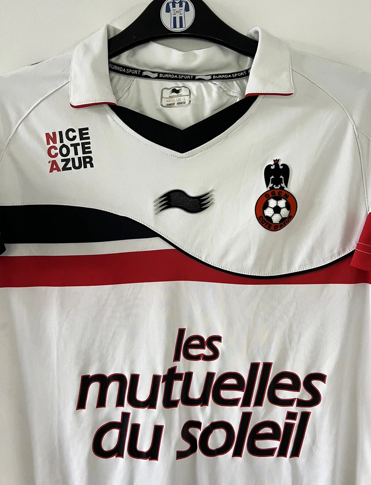 Maillot de foot vintage extérieur blanc de l'OGC Nice porté par Fabian Monzon lors de la saison 2011/2012. On peut retrouver l'équipementier Burrda Sport et le sponsor Mutuelle du Soleil. Le maillot est floqué du numéro 18 Fabian Monzon. Il s'agit d'un maillot authentique d'époque.