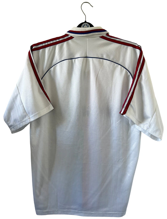 Maillot de foot vintage domicile blanc, bleu et rouge de l'Olympique Lyonnais de la saison 1998/2000. On peut retrouver l'équipementier Adidas et le sponsor Infogrames. Il s'agit d'un maillot authentique d'époque.