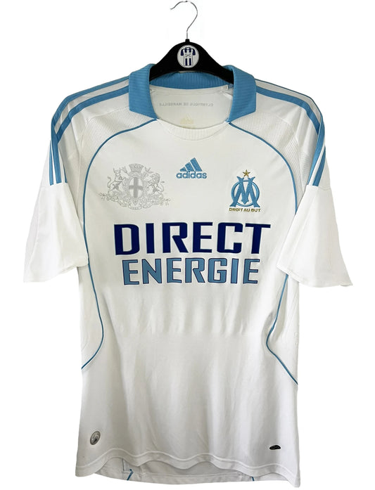 Maillot de foot vintage domicile blanc et bleu de l'om de la saison 2008-2009. On peut retrouver l'équipementier adidas, le sponsor direct energie, groupama et nasuba express. Le maillot est floqué du numéro 22 Wiltord. Il s'agit d'un maillot authentique d'époque comportant l'étiquette 314635