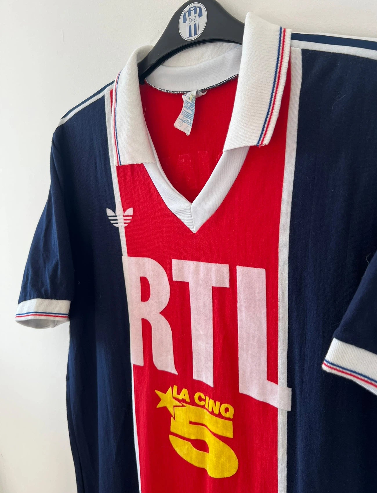 Maillot de foot vintage domicile bleu et rouge du PSG de la saison 1987/1988. On peut retrouver l'équipementier Adidas et le sponsor RTL, Canal + et La Cinq. Il s'agit d'un maillot authentique d'époque.