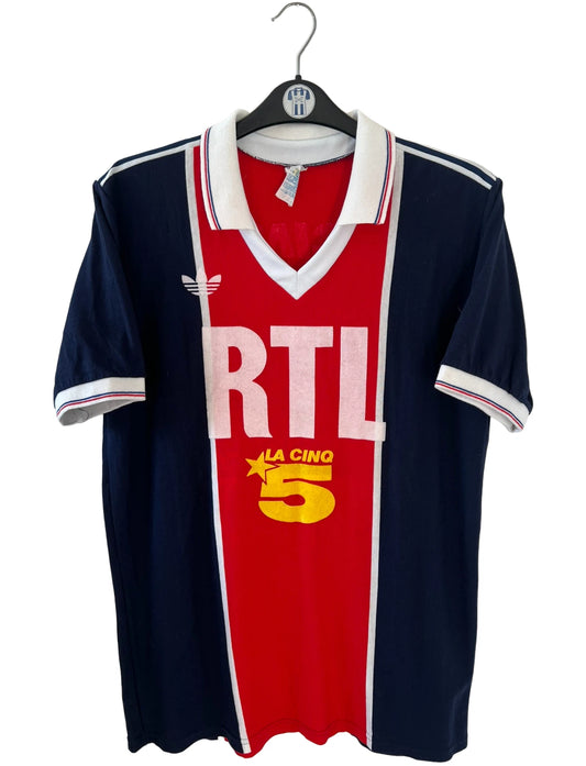Maillot de foot vintage domicile bleu et rouge du PSG de la saison 1987/1988. On peut retrouver l'équipementier Adidas et le sponsor RTL, Canal + et La Cinq. Il s'agit d'un maillot authentique d'époque.