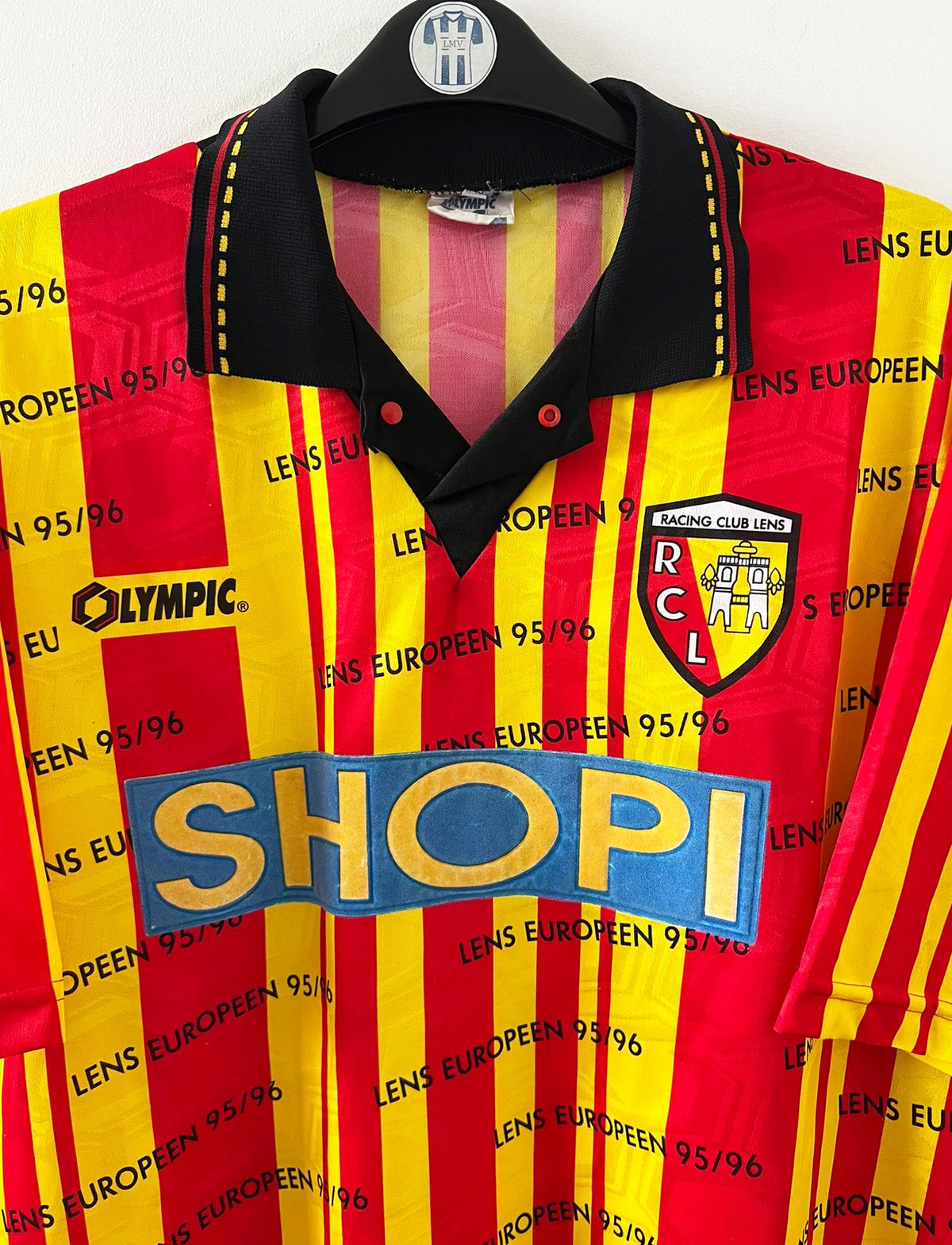 Maillot de foot vintage domicile jaune et rouge du RC Lens 1995/1996. Il s'agit d'une version Lens Européen 95/96. On peut retrouver l'équipementier Olympic et le sponsor Shopi. Il s'agit d'un maillot authentique d'époque.