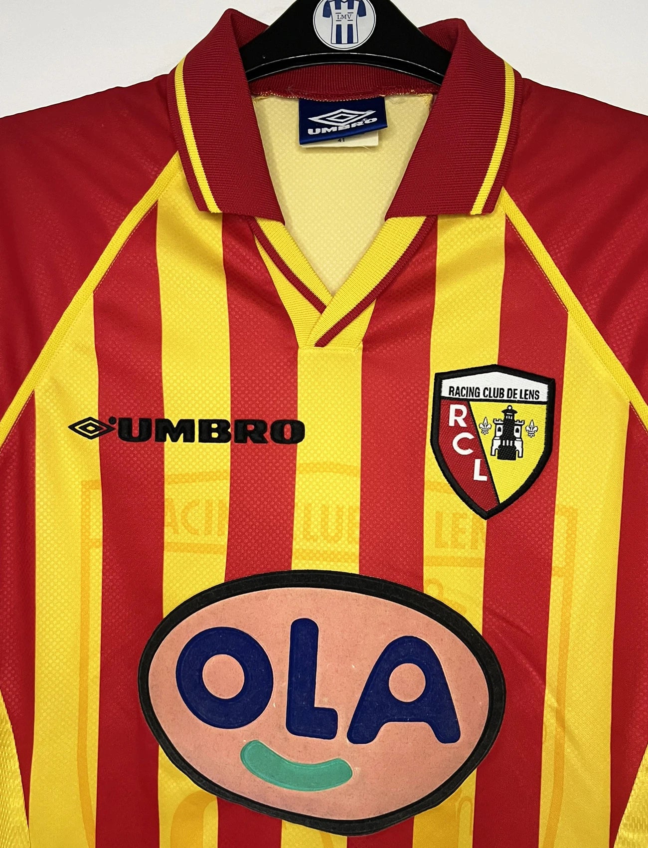Maillot de foot vintage domicile jaune et rouge du RC Lens de la saison 1998/1999. On peut retrouver l'équipementier Umbro et le sponsor OLA. Il s'agit d'un maillot authentique d'époque.