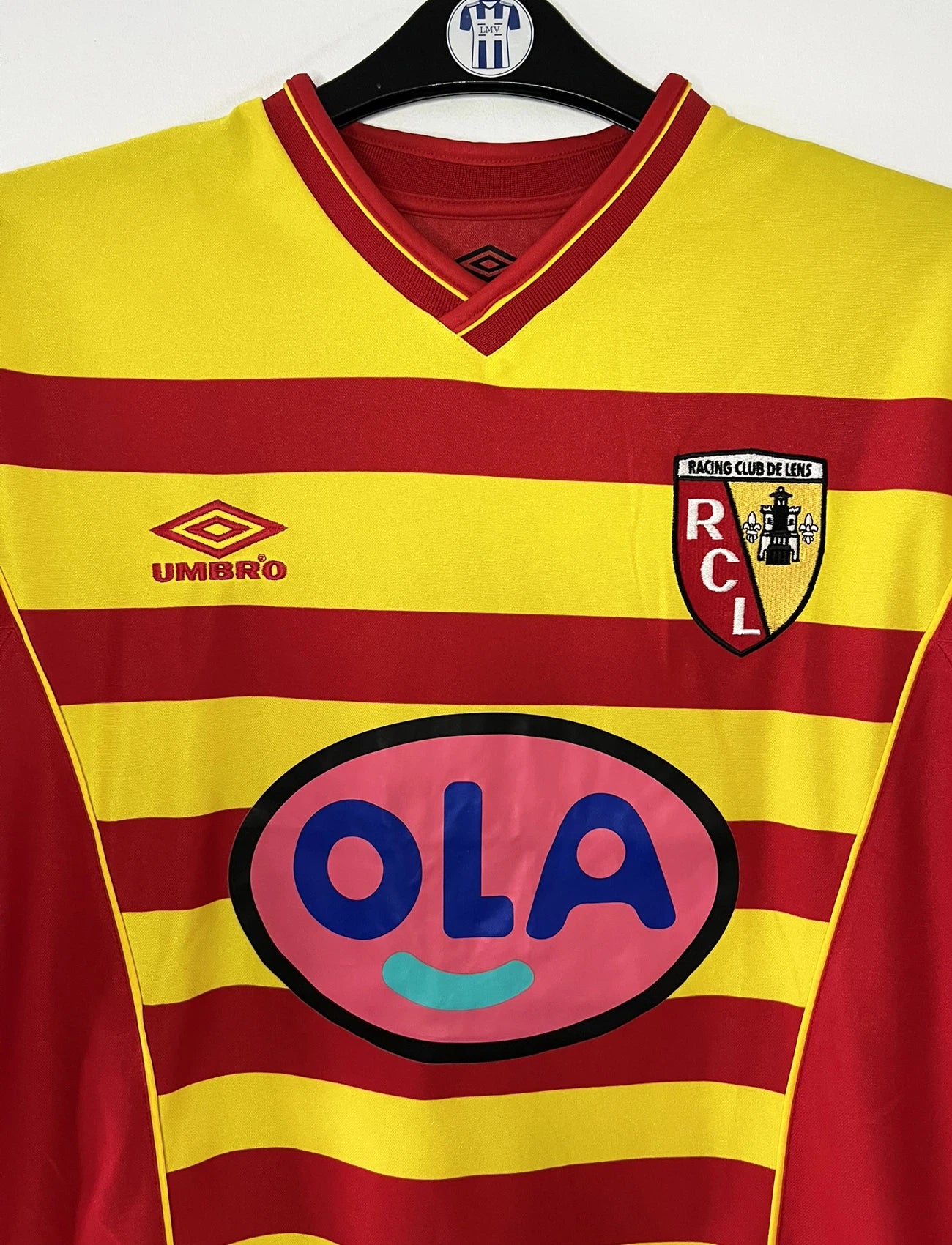 Maillot de foot vintage domicile rouge et jaune du RC Lens de la saison 2000/2001. On peut retrouver l'équipementier Umbro et le sponsor OLA. Il s'agit d'un maillot authentique d'époque.