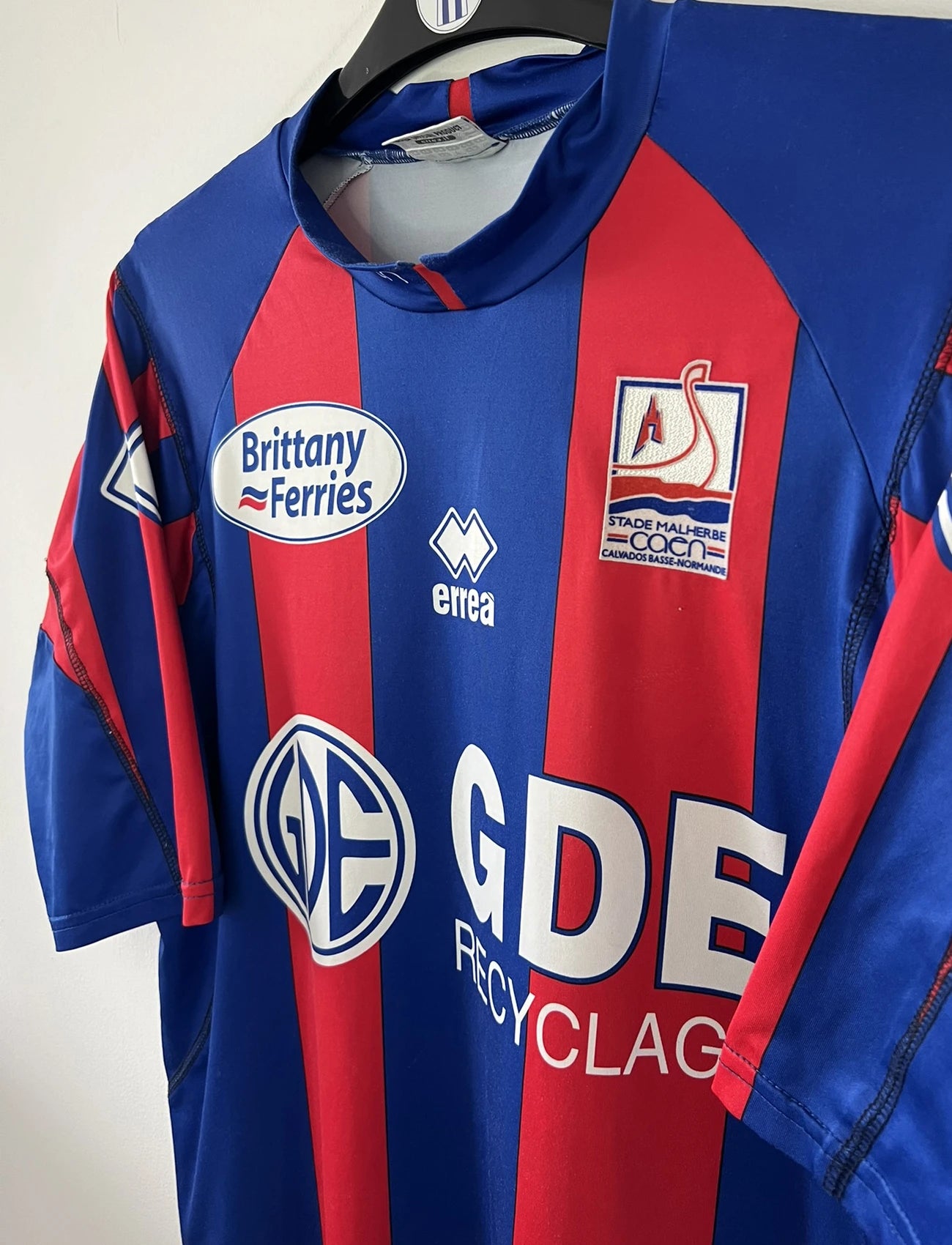 Maillot de foot vintage domicile bleu et rouge du SM Caen de la saison 2006/2007. On peut retrouver l'équipementier Errea et le sponsor Brittany Ferries et GDE. Il s'agit d'un maillot authentique d'époque.