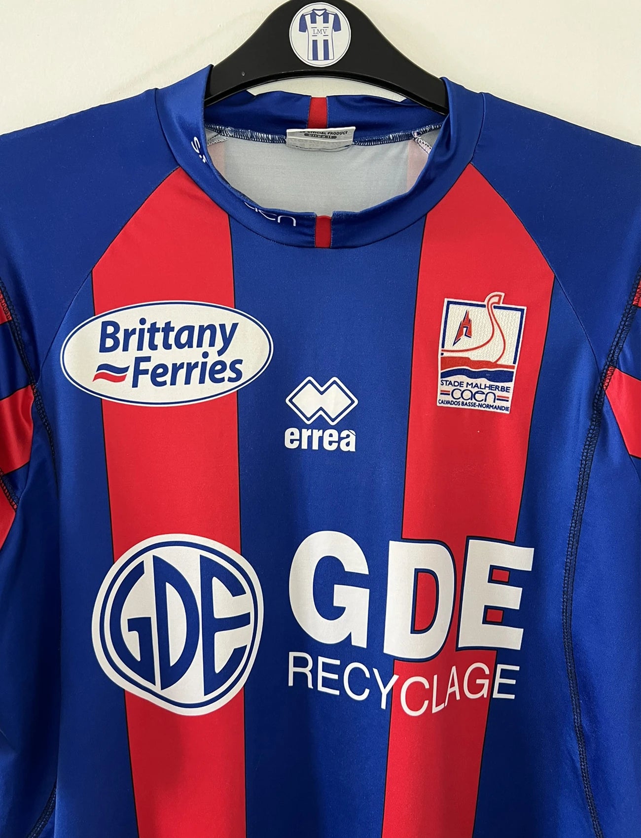 Maillot de foot vintage domicile bleu et rouge du SM Caen de la saison 2006/2007. On peut retrouver l'équipementier Errea et le sponsor Brittany Ferries et GDE. Il s'agit d'un maillot authentique d'époque.