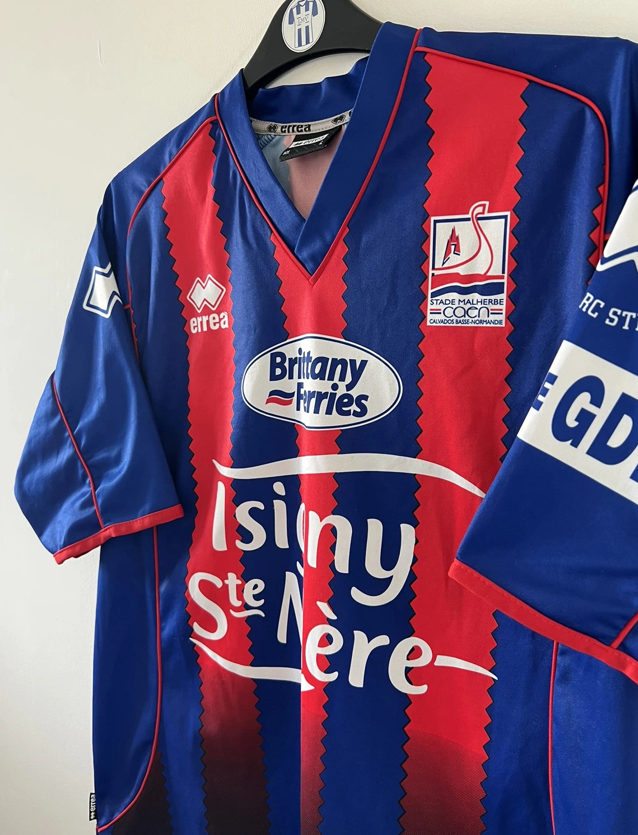 Maillot de foot vintage domicile bleu et rouge du SM Caen édité lors de la finale de la coupe de la Ligue de la saison 2004/2005. On peut retrouver l'équipementier errea et le sponsor isigny sainte mère. Il s'git d'un maillot authentique d'époque.