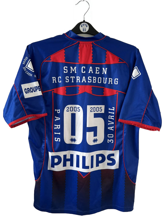 Maillot de foot vintage domicile bleu et rouge du SM Caen édité lors de la finale de la coupe de la Ligue de la saison 2004/2005. On peut retrouver l'équipementier errea et le sponsor isigny sainte mère. Il s'git d'un maillot authentique d'époque.