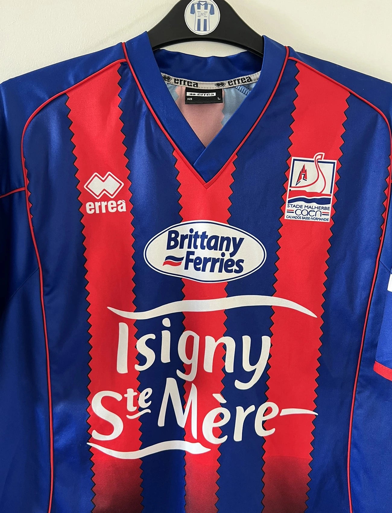 Maillot de foot vintage domicile bleu et rouge du SM Caen édité lors de la finale de la coupe de la Ligue de la saison 2004/2005. On peut retrouver l'équipementier errea et le sponsor isigny sainte mère. Il s'git d'un maillot authentique d'époque.