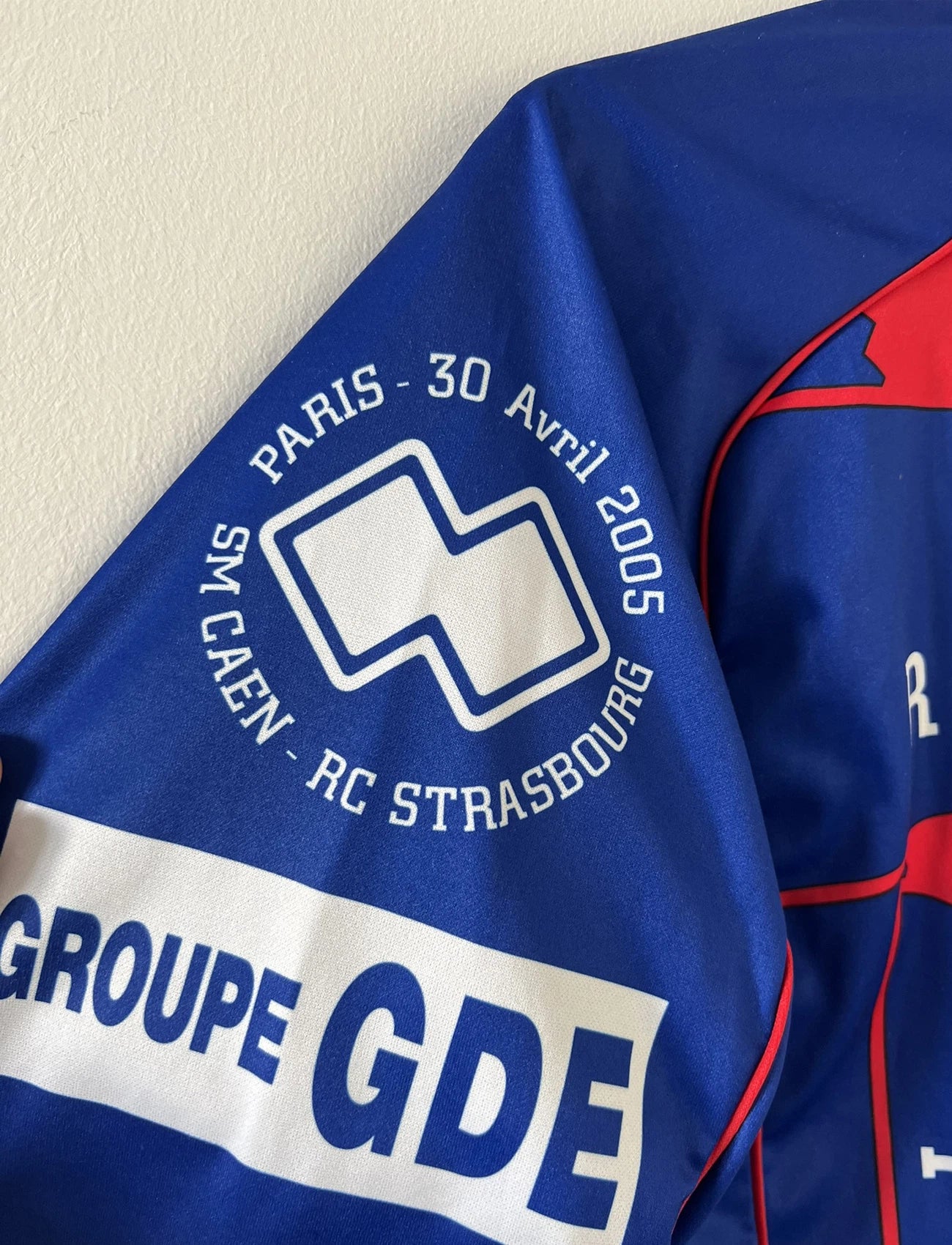 Maillot de foot vintage domicile bleu et rouge du SM Caen édité lors de la finale de la coupe de la Ligue de la saison 2004/2005. On peut retrouver l'équipementier errea et le sponsor isigny sainte mère. Il s'git d'un maillot authentique d'époque.