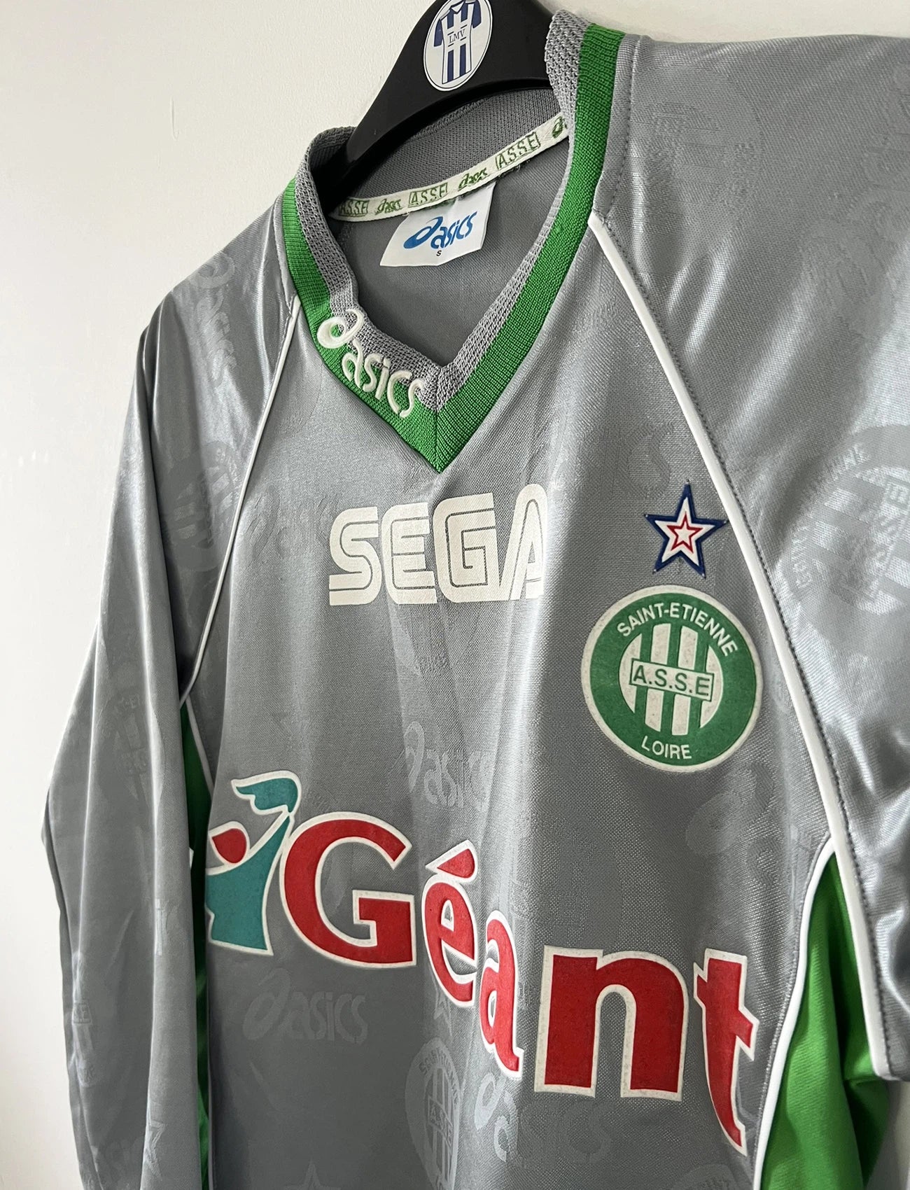 Maillot de foot vintage extérieur gris de l'AS Saint Etienne de la saison 1999/2000. On peut retrouver l'équipementier Asics et les sponsor, Sega, Géant Casino, Dreamcast. Il s'agit d'un maillot authentique d'époque.