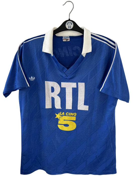 Maillot de foot vintage extérieur bleu du PSG saison 1988/1989. On peut retrouver l'équipementier Adidas et le sponsor RTL, La Cinq et Canal +. Il s'agit d'un maillot authentique d'époque.