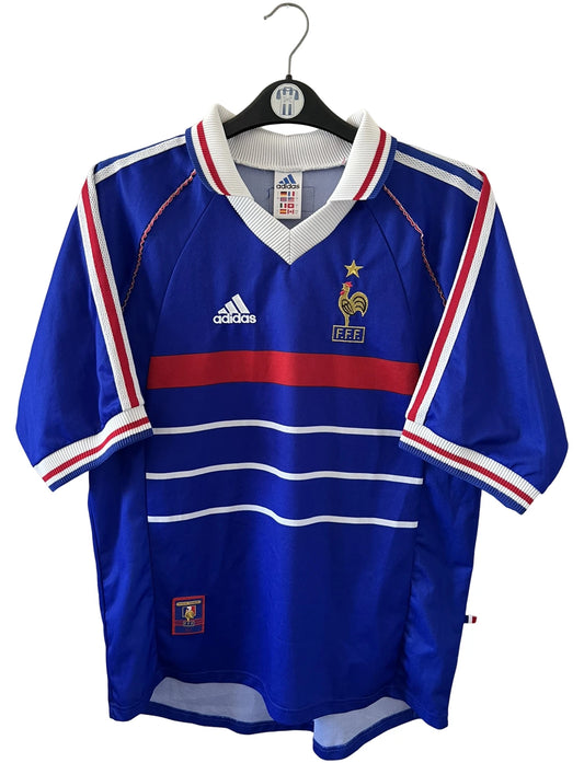 Maillot foot vintage domicile equipe de france 1998 bleu blanc et rouge. On peut retrouver l'équipementier adidas. Il s'agit d'un maillot authentique d'époque. Le maillot est floqué du numéro 10 Zinedine Zidane et comporte également sa signature avec la mention "pour toi Zinedine Zidane"