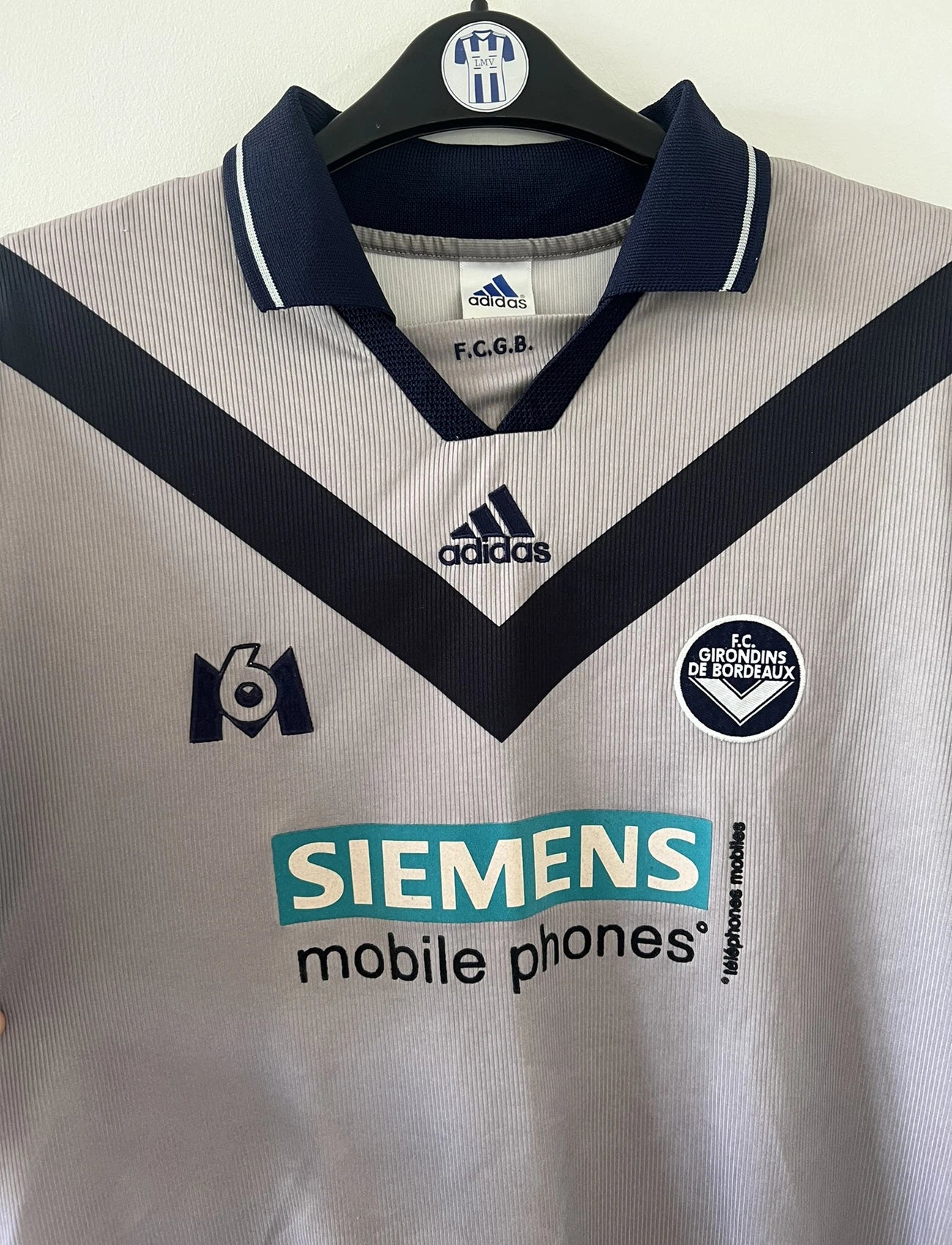 Maillot de foot vintage extérieur gris et bleu des girondins de bordeaux de la saison 2000/2001. On peut retrouver l'équipementier adidas et le sponsor Siemens et M6. Il s'agit d'un maillot authentique d'époque comportant l'étiquette 693826.