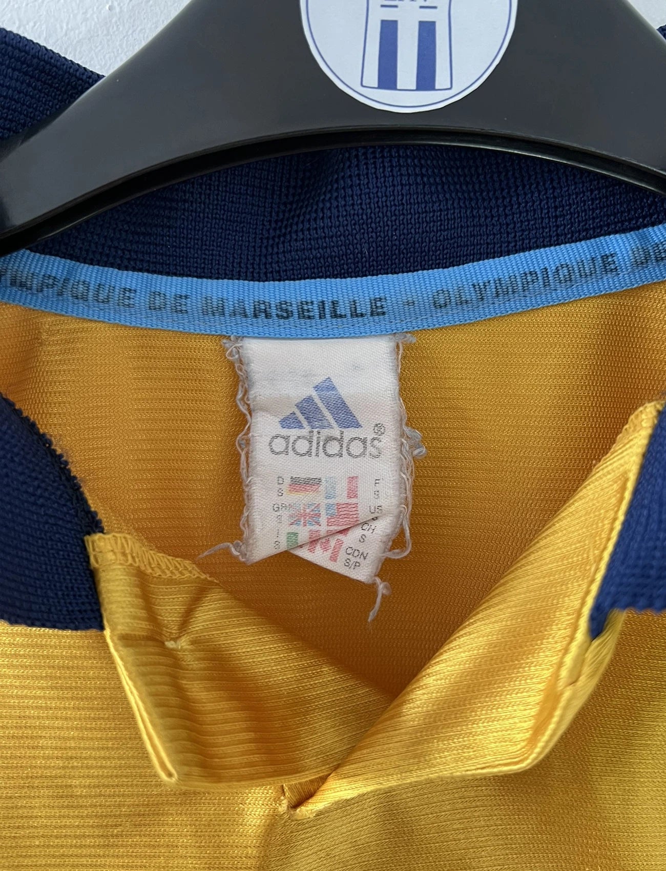 Maillot de foot vintage third de l'OM de la saison 1998-1999. Il s'agit du maillot édité pour le centenaire du club. Le maillot est de couleur dorée et bleu. On peut retrouver l'équipementier adidas et le sponsor ericsson. Il s'agit d'un maillot authentique d'époque.