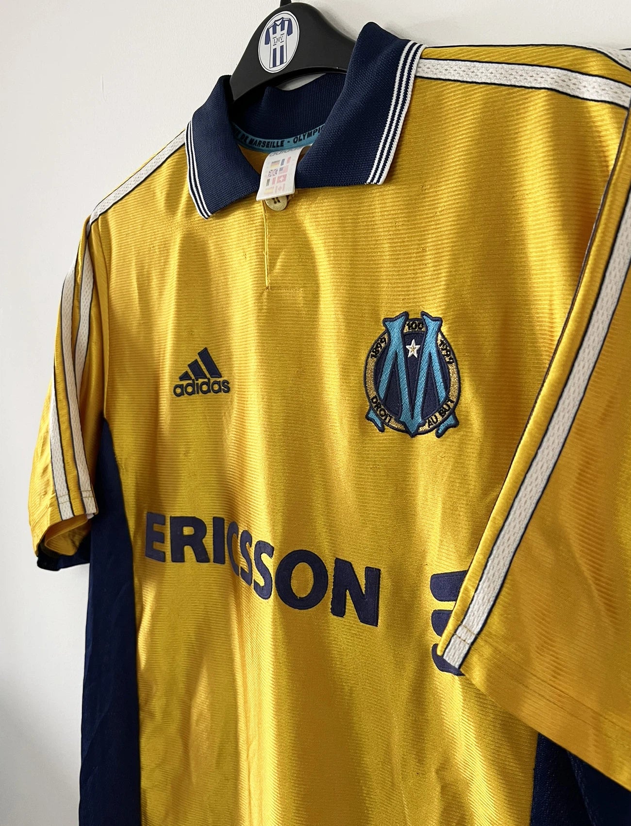 Maillot de foot vintage third de l'OM de la saison 1998-1999. Il s'agit du maillot édité pour le centenaire du club. Le maillot est de couleur dorée et bleu. On peut retrouver l'équipementier adidas et le sponsor ericsson. Il s'agit d'un maillot authentique d'époque.