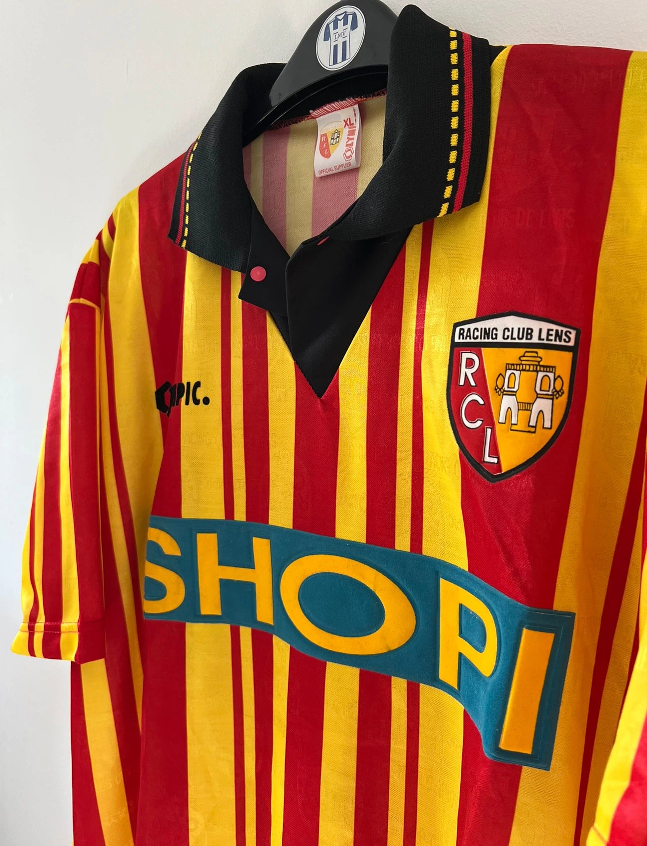 Maillot de foot vintage domicile rouge et jaune du RC Lens de la saison 1995/1996. On peut retrouver l'équipementier Olympic et le sponsor Shopi. Il s'agit d'un maillot authentique d'époque.