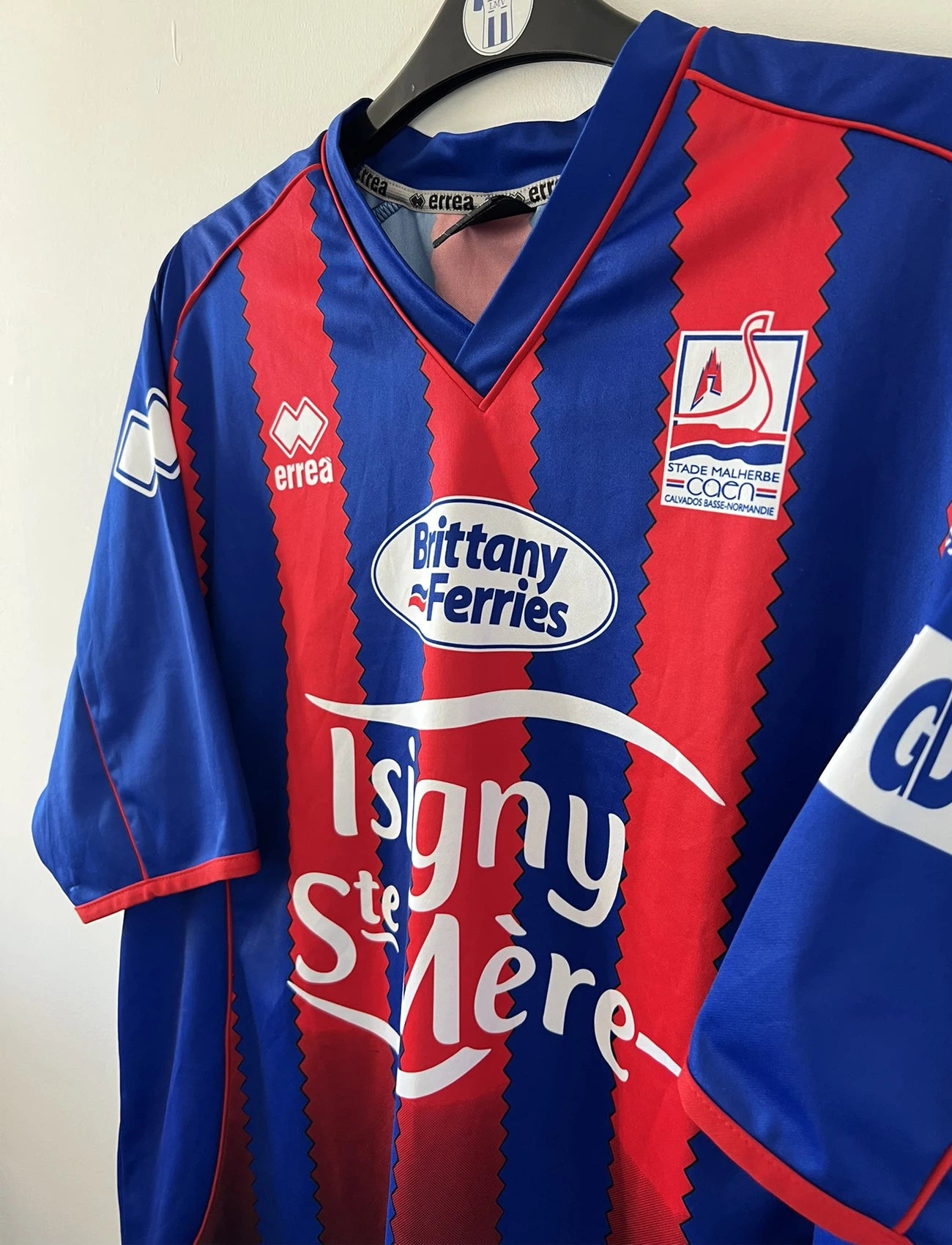 Maillot de foot vintage domicile bleu et rouge du SM Caen édité lors de la finale de la coupe de la Ligue de la saison 2004/2005. On peut retrouver l'équipementier errea et le sponsor isigny sainte mère. Il s'git d'un maillot authentique d'époque.