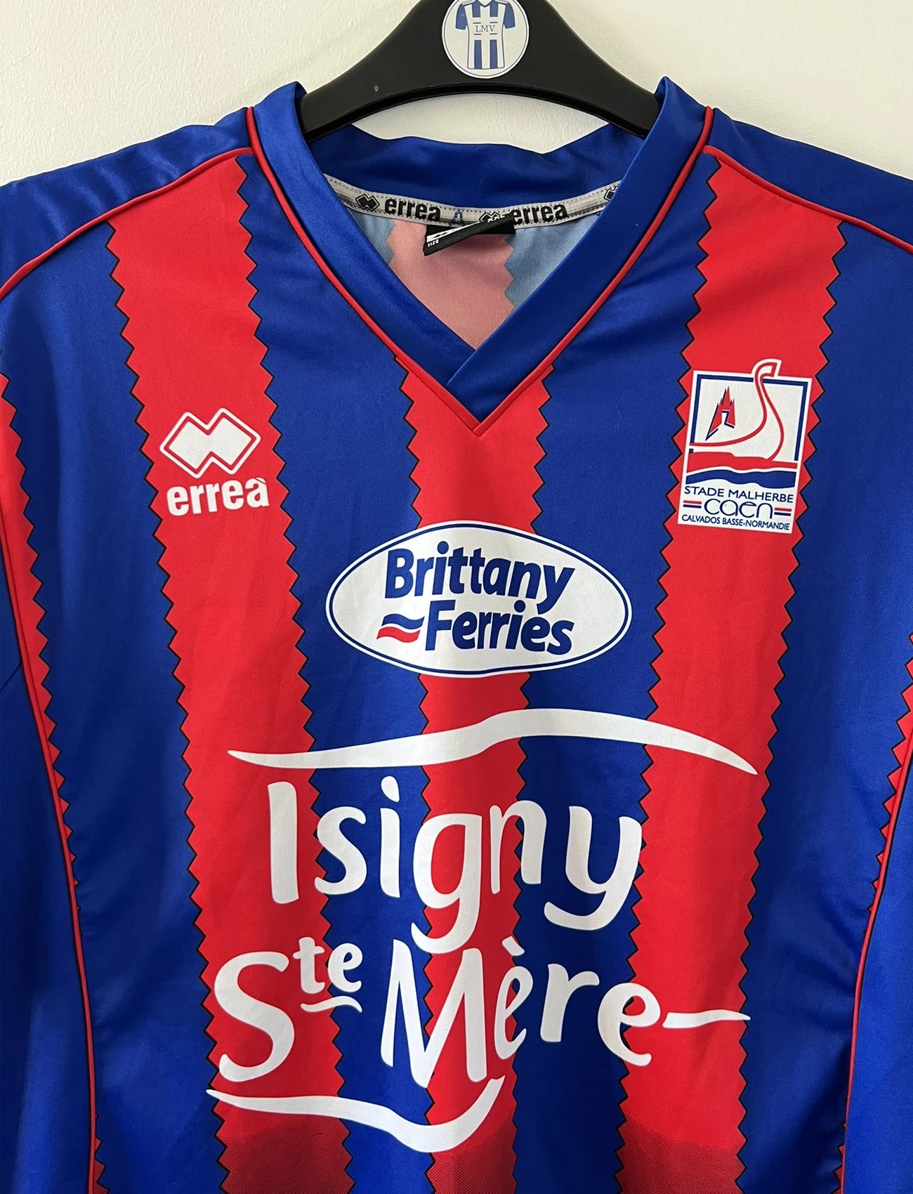 Maillot de foot vintage domicile bleu et rouge du SM Caen édité lors de la finale de la coupe de la Ligue de la saison 2004/2005. On peut retrouver l'équipementier errea et le sponsor isigny sainte mère. Il s'git d'un maillot authentique d'époque.