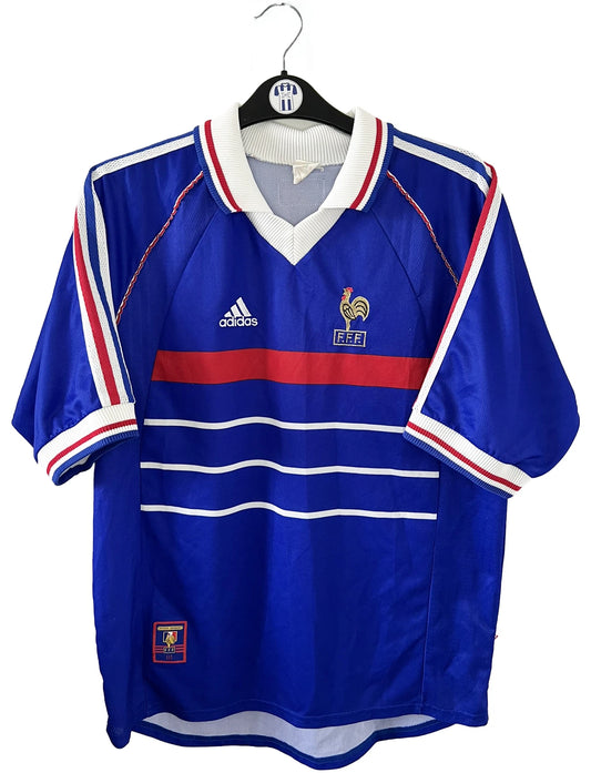 Maillot de foot vintage bleu, blanc et rouge de l'équipe de france 1998. On peut retrouver l'équipementier adidas. Il s'agit d'un maillot authentique édité avant la finale de la coupe du monde car celui-ci ne possède pas l'étoile. Le maillot est floqué du numéro 10 Zidane