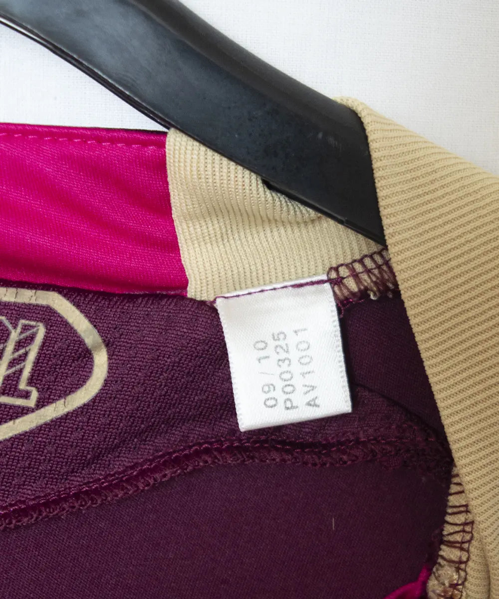 Maillot extérieur de l'ol de la saison 2010-2011. Le maillot est de couleur violet et dorée. On peut retrouver l'équipementier adidas et le sponsor everest poker. Sur cette photo on peut voir l'étiquette d'authenticité comportant les numéros P00325