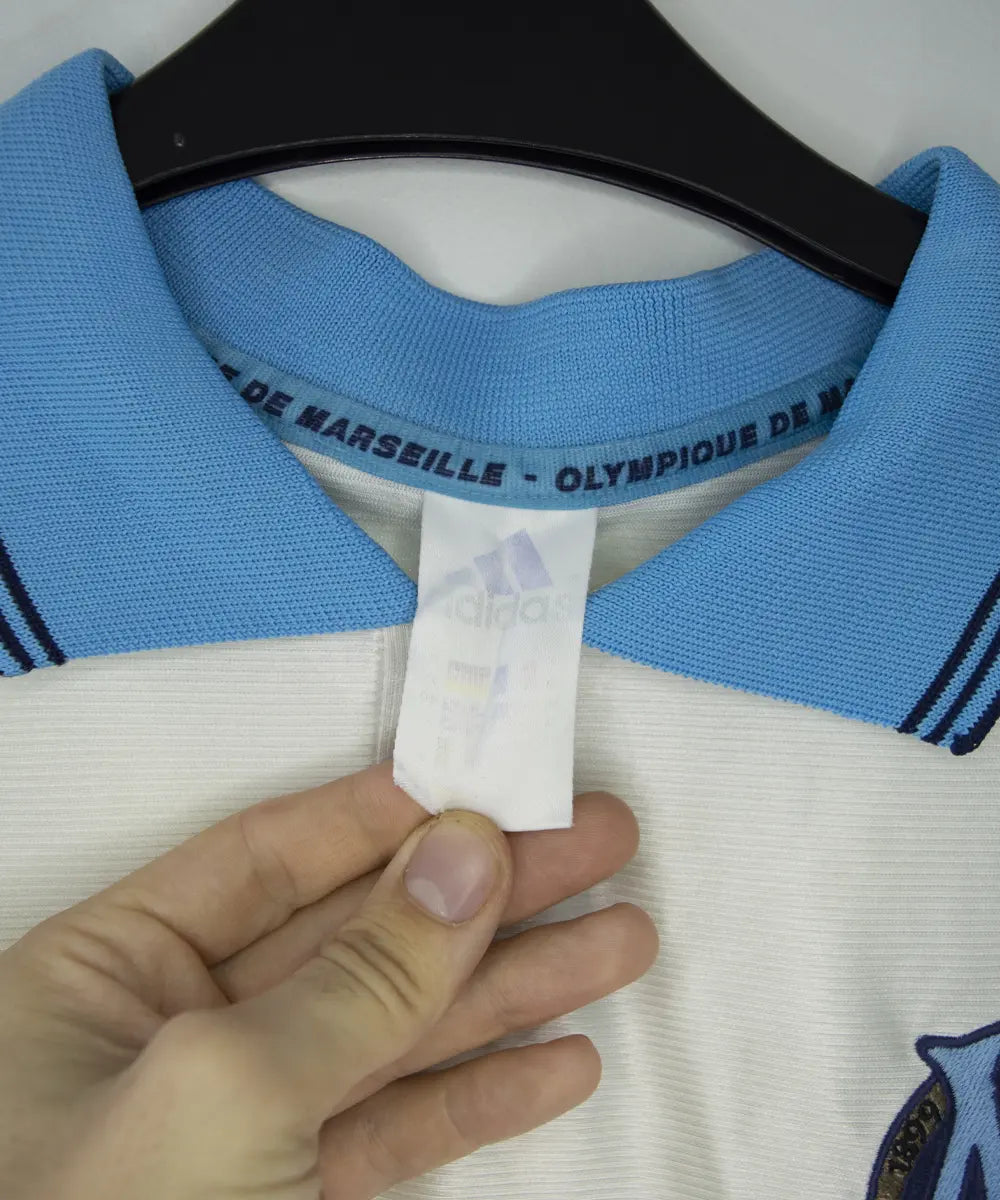 Maillot domicile de l'om de la saison 1998-1999. Le maillot est de couleur blanc et bleu. On peut retrouver l'équipementier adidas et le sponsor ericsson
