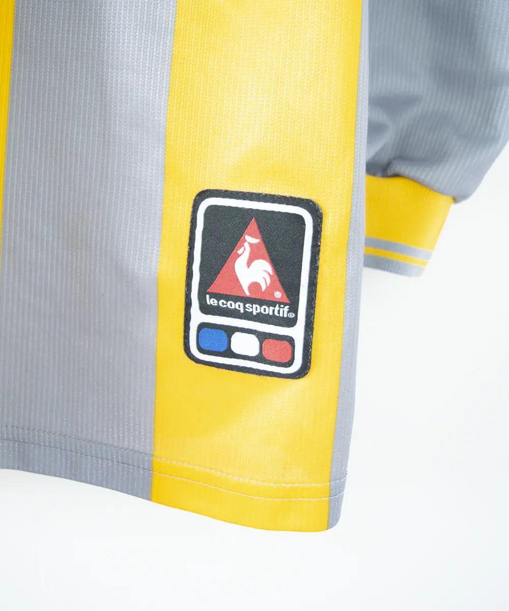 Maillot du SM Caen de la saison 2000-2001. Le maillot est de couleur gris et jaune. On peut retrouver l'équipementier le coq sportif, le sponsor infonie et le sponsor isigny sainte mère. On peut aussi retrouver l'ancien patch LNF. Le maillot est floqué du numéro 20 Faderne