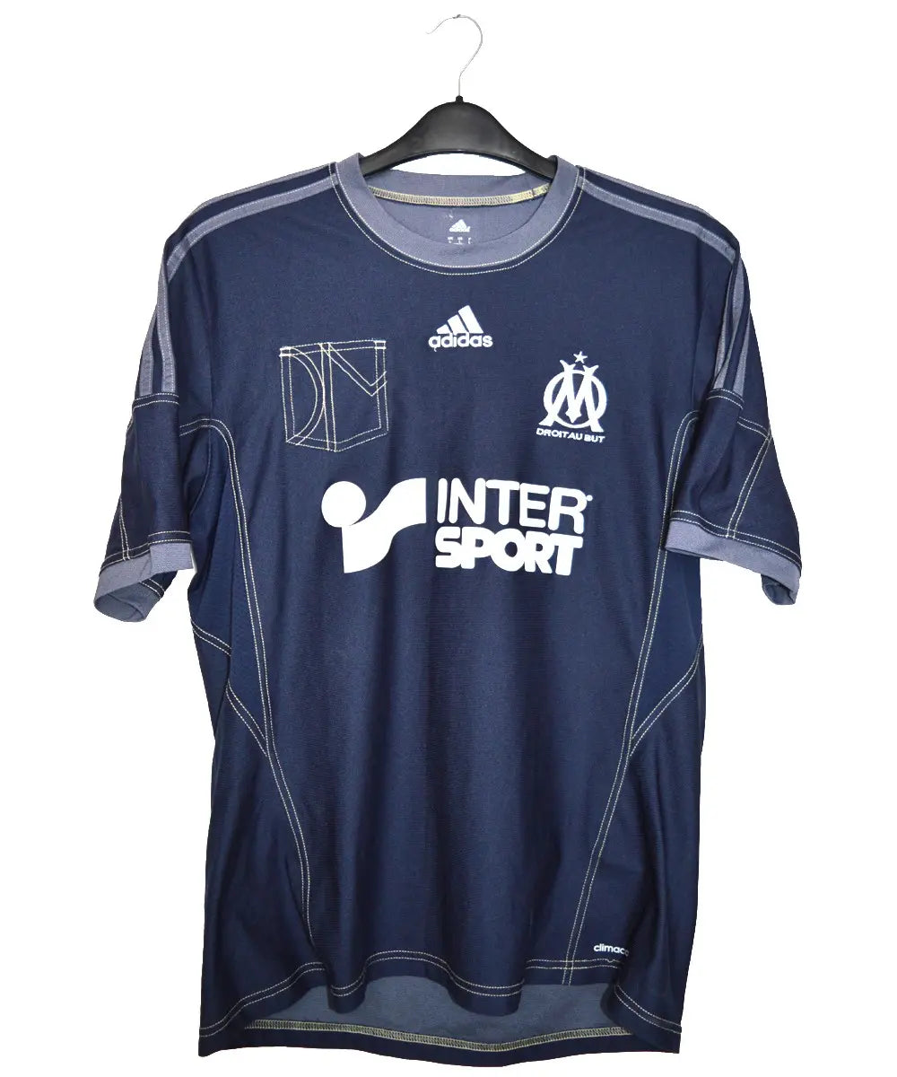 Maillot extérieur de l'om noir et blanc porté lors de la saison 2013-2014. On peut retrouver sur le maillot le sponsor intersport et l'équipementier adidas.