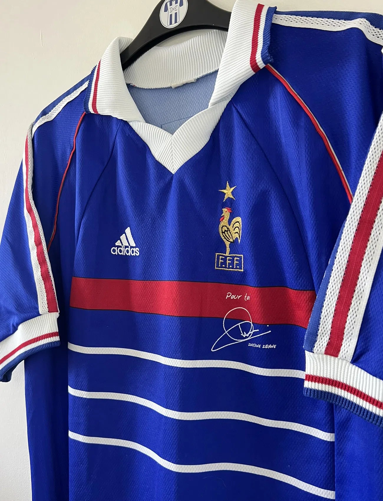 Maillot de foot vintage bleu blanc et rouge domicile de l'équipe de France 1998. On peut retrouver le sponsor adidas. On peut voir le coq avec l'étoile avec la signature "pour toi" de Zinedine Zidane. Il s'agit d'un maillot authentique.