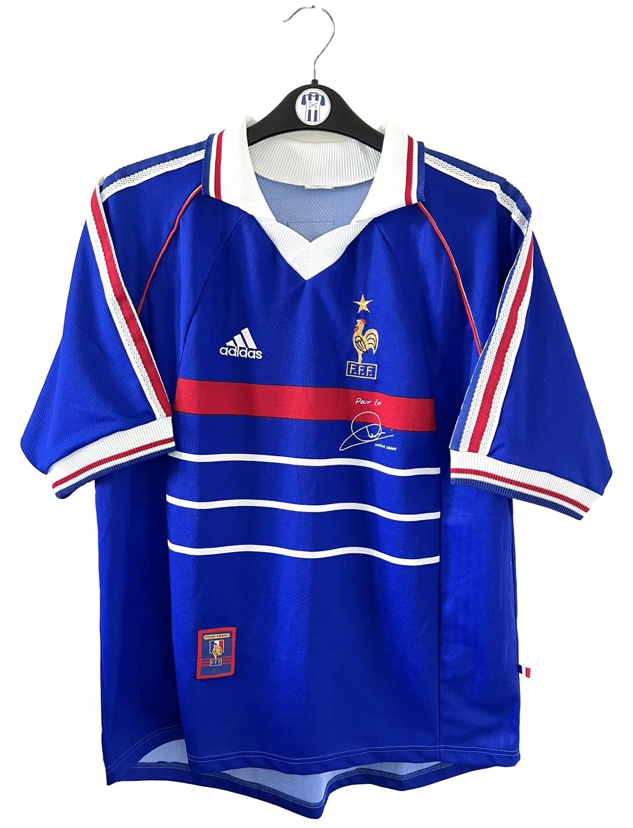 Maillot de foot vintage bleu blanc et rouge domicile de l'équipe de France 1998. On peut retrouver le sponsor adidas. On peut voir le coq avec l'étoile avec la signature "pour toi" de Zinedine Zidane. Il s'agit d'un maillot authentique.