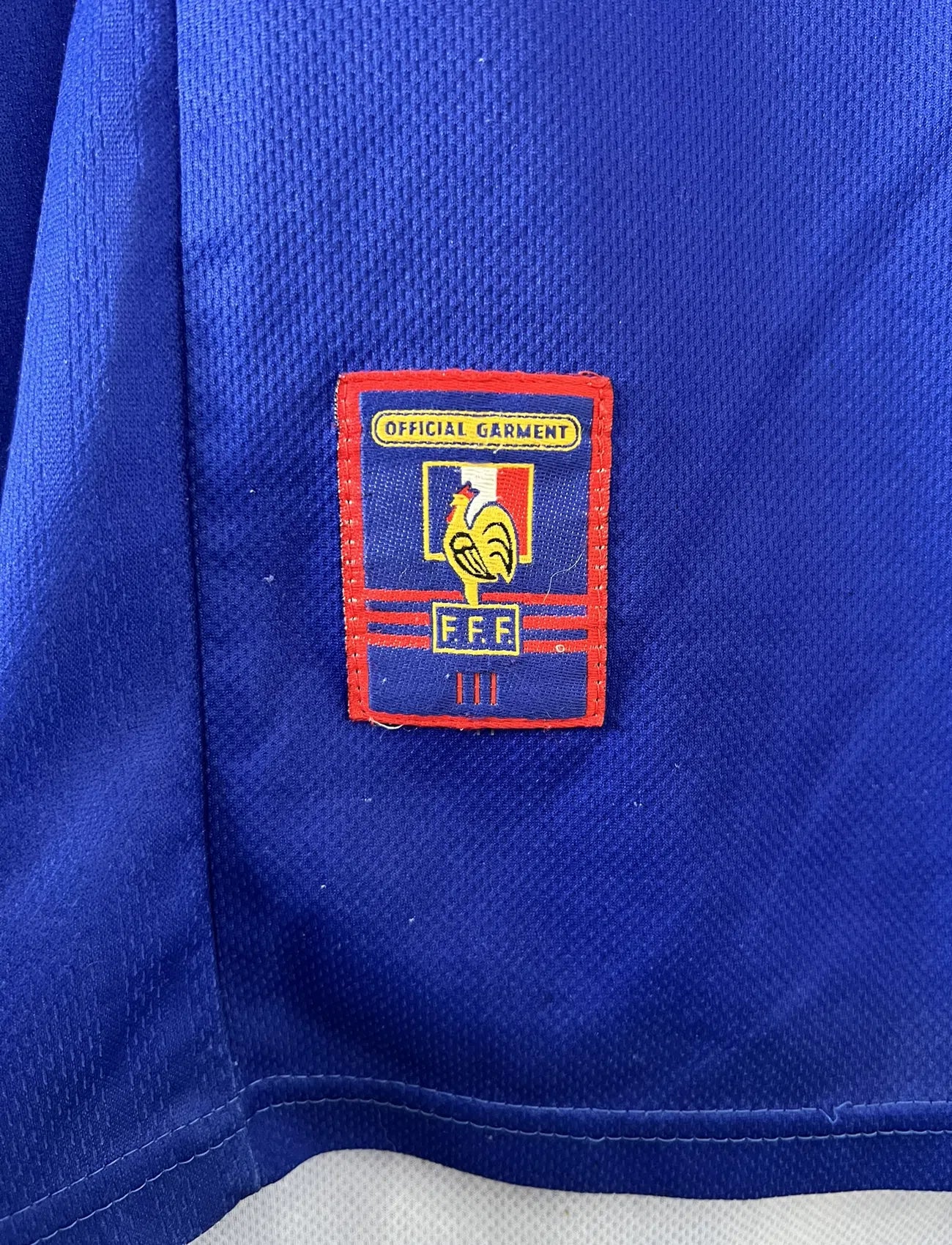 Maillot de foot vintage de l'équipe de france 98 bleu blanc et rouge. On peut retrouver l'équipementier adidas et le coq avec l'étoile. Il s'agit d'un maillot authentique édité lors de la coupe du monde 1998.