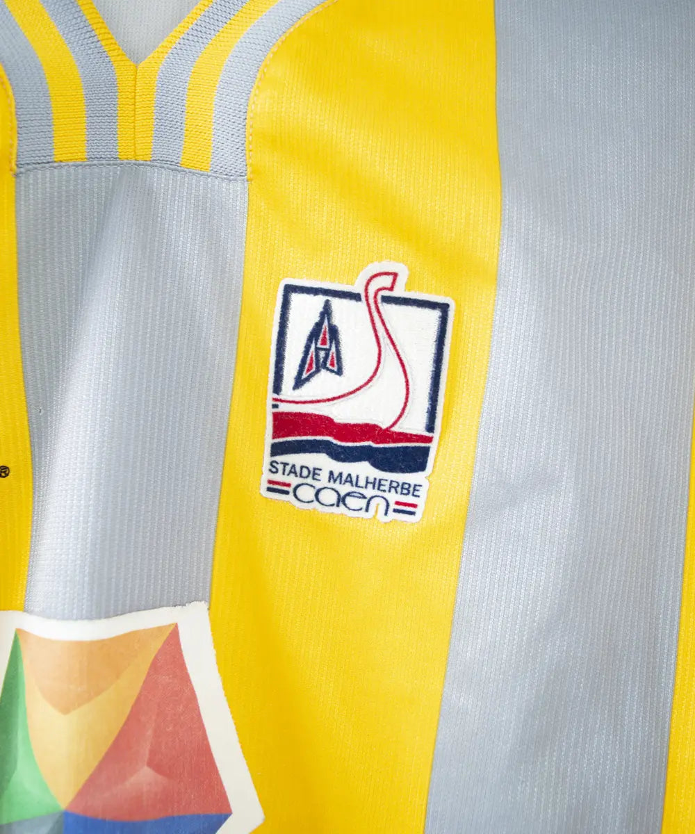 Maillot du SM Caen de la saison 2000-2001. Le maillot est de couleur gris et jaune. On peut retrouver l'équipementier le coq sportif, le sponsor infonie et le sponsor isigny sainte mère. On peut aussi retrouver l'ancien patch LNF. Le maillot est floqué du numéro 20 Faderne